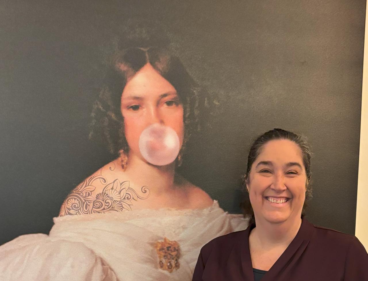 First Community UCC Dallas Lead Pastor Rev Melissa Ashmore in front of portrait of woman blowing bubble gum bubble