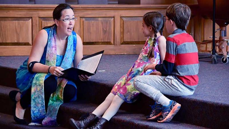 Pastor Sarah with two children sitting on the steps in the sanctuary.